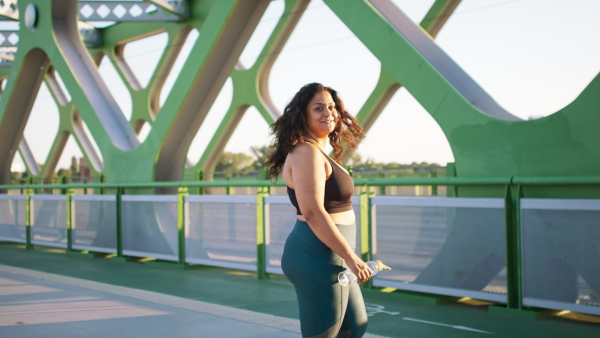 A young overweight woman in sports clothes turning and looking at camera outdoors in bridge.