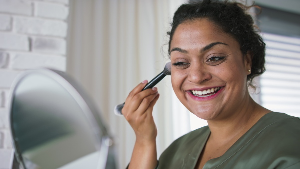 A beautiful young overweight woman indoors at home, applying make-up.