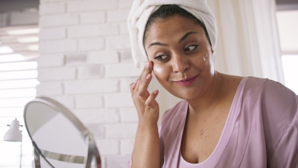 A beautiful young overweight woman indoors at home, applying face cream.