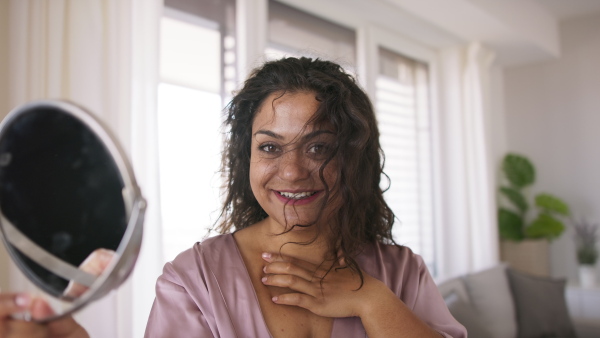 A beautiful young overweight woman indoors at home, looking at mirror.