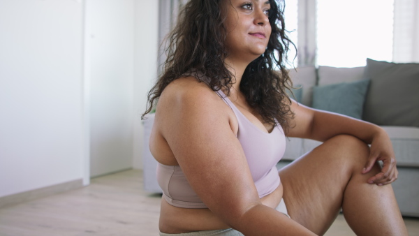 A young overweight woman indoors at home, exercising with dumbbell.