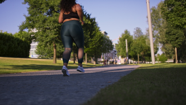 A rear view of young overweight woman jogging outdoors in street.