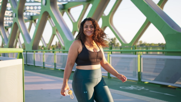 A young overweight woman in sports clothes turning and looking at camera outdoors in bridge.