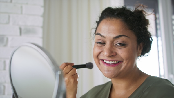 A close up of beautiful young overweight woman indoors at home, applying make-up and looking at camera