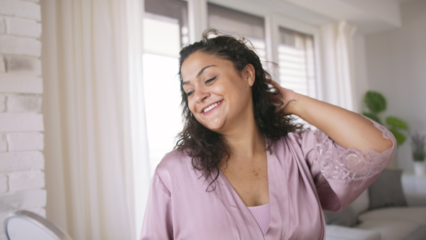 A beautiful young overweight woman indoors at home, looking at mirror.