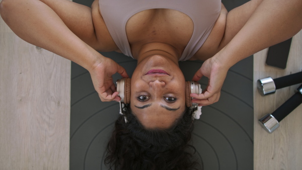 A top view of beautiful young overweight woman lying on floor indoors at home, listening music