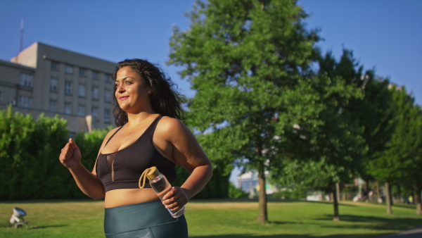 A young overweight woman in sports clothes walking outdoors in street.