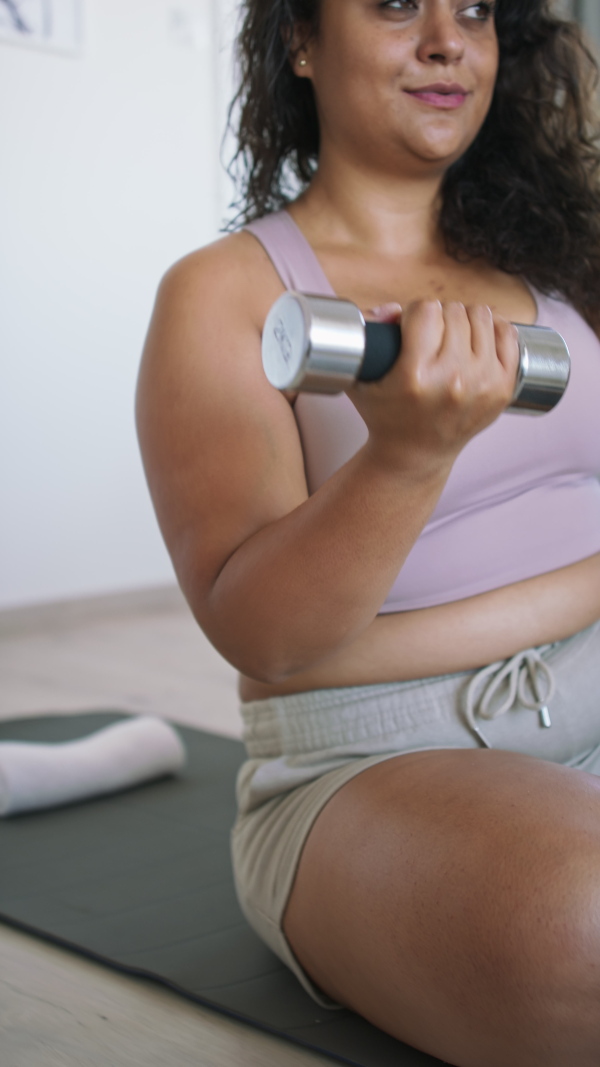 A vertical footage of happy young overweight woman indoors at home, exercising.