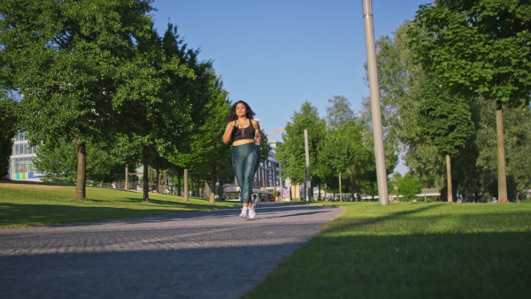 A young overweight woman in sports clothes jogging outdoors in street.