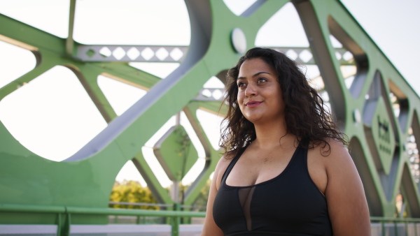 A young overweight woman in sports clothes walking outdoors in bridge.