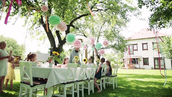 Group of small children sitting at the table outdoors on garden party in summer, eating. Slow motion.