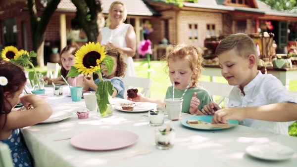 Group of small children sitting at the table outdoors on garden party in summer, eating. Slow motion.