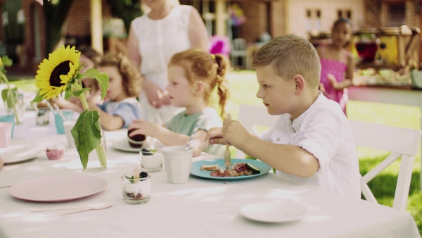 Group of small children sitting at the table outdoors on garden party in summer, eating.