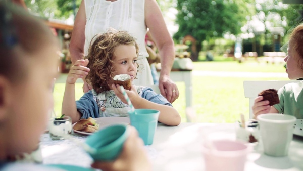 Group of small children sitting at the table outdoors on garden party in summer, eating. Slow motion.