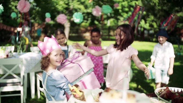 A birthday party of small girl outdoors in garden in summer, celebration concept. Slow motion.