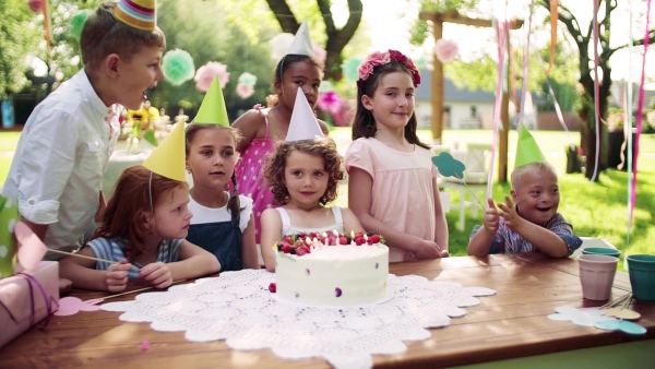 Down syndrome child with friends on birthday party outdoors in garden in summer. Slow motion.