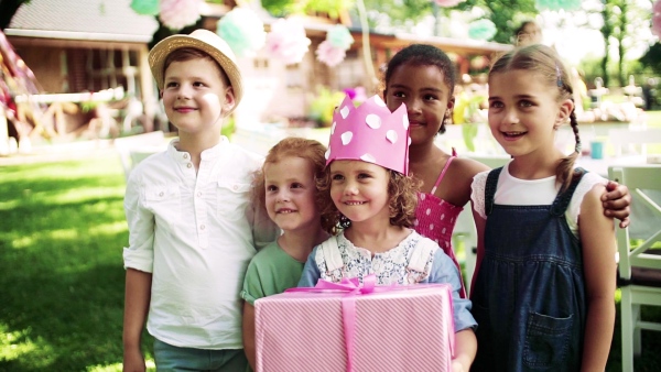 Portrait of small girl with friends and presents outdoors in garden in summer. Slow motion.