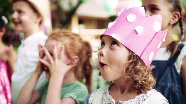 A portrait of children standing on birthday party in garden in summer, celebration concept. Slow motion.