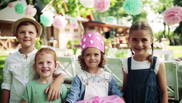 Portrait of small girl with friends and presents outdoors in garden in summer. Slow motion.