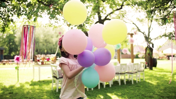 A small girl playing with balloons outdoors on birthday garden party in summer. Slow motion.