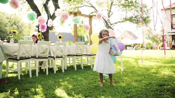 A small girl playing with balloons outdoors on birthday garden party in summer. Slow motion.