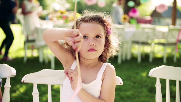 A front view of small girl on birthday party outdoors in garden in summer. Slow motion.