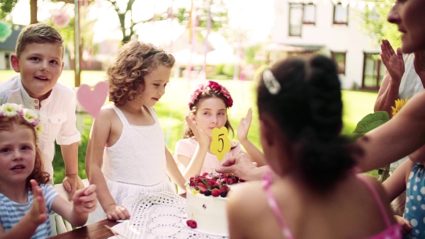 A portrait of children with cake standing around table on birthday party in garden in summer. Slow motion.