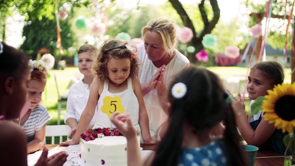 A birthday party of small girl outdoors in garden in summer, celebration concept. Slow motion.