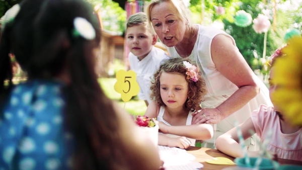 A birthday party of small girl outdoors in garden in summer, celebration concept. Slow motion.