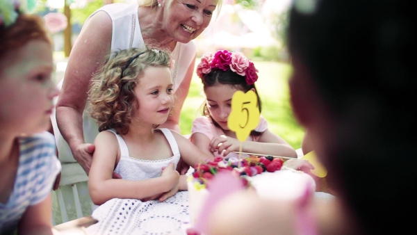 A portrait of children with cake standing around table on birthday party in garden in summer. Slow motion.