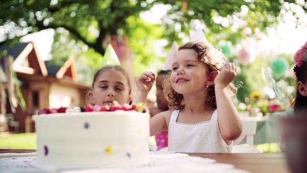 A birthday party of small girl outdoors in garden in summer, celebration concept. Slow motion.