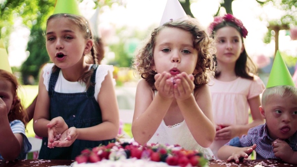 Down syndrome child with friends on birthday party outdoors in garden in summer. Slow motion.