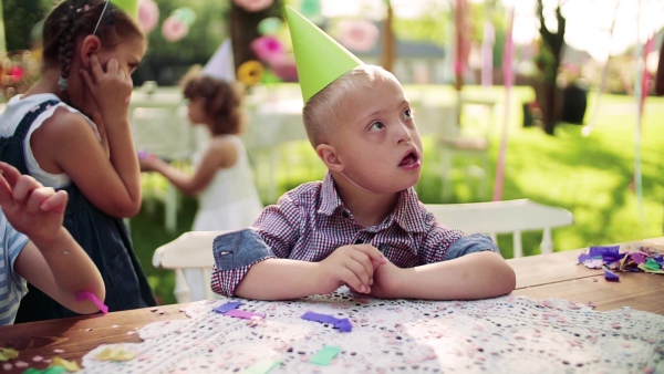 Down syndrome child with friends on birthday party outdoors in garden in summer. Slow motion.