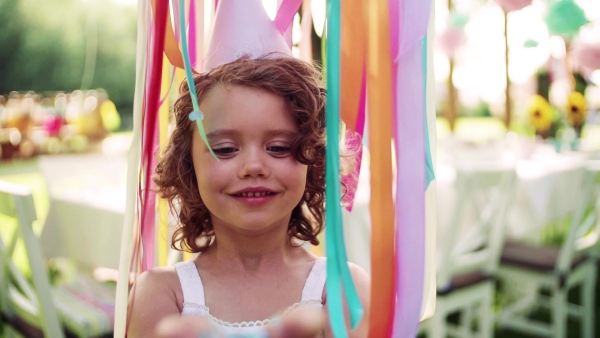 A front view of small girl on birthday party outdoors in garden in summer. Slow motion.