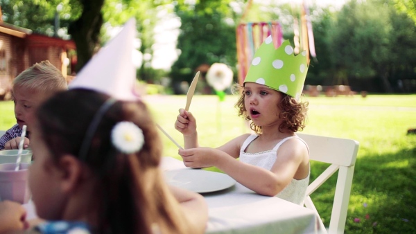 Group of small children sitting at the table outdoors on garden party in summer, waiting for cake.