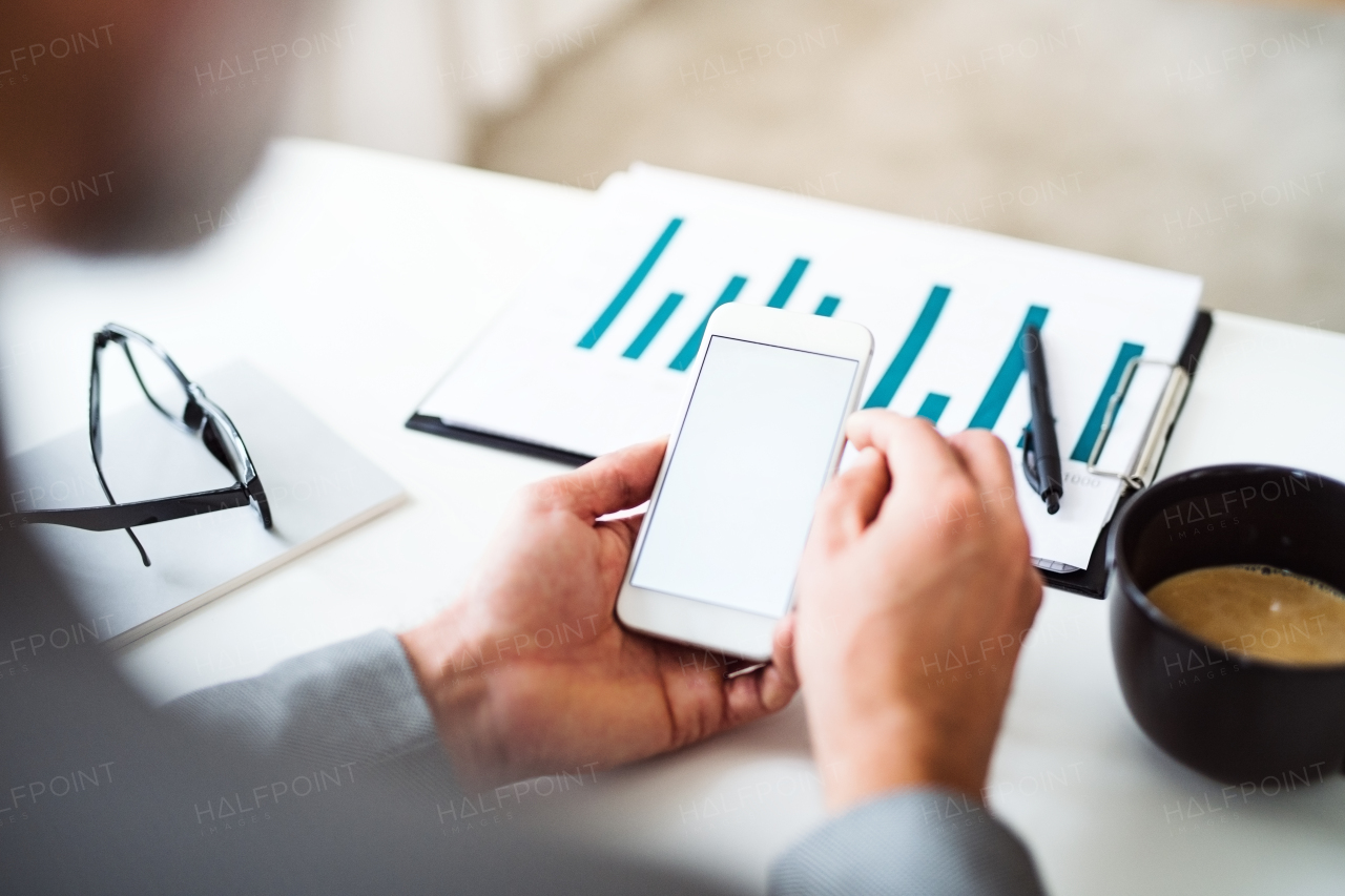 A midsection of businessman with coffee sitting at the table, using smartphone. Copy space.