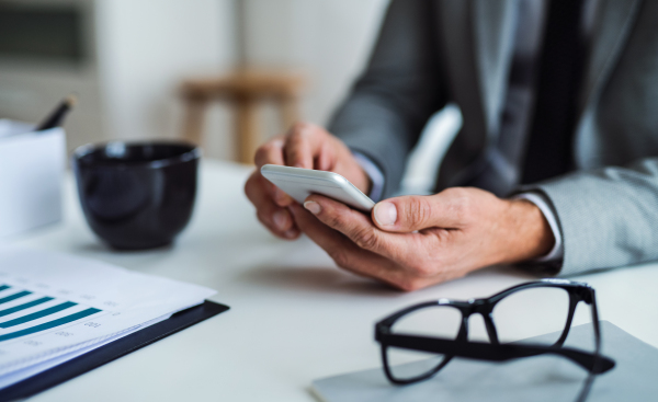 A midsection of businessman with smartphone, glasses and laptop sitting at the table in an office, working. Copy space.