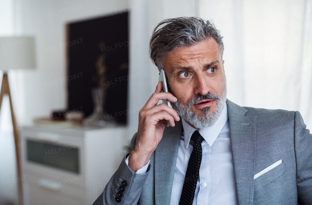 A sad and frustrated businessman with smartphone standing in an office, hearing bad news.