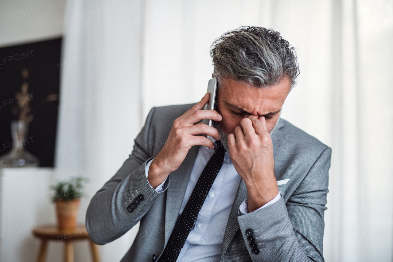 A sad and frustrated businessman with smartphone standing in an office, hearing bad news.