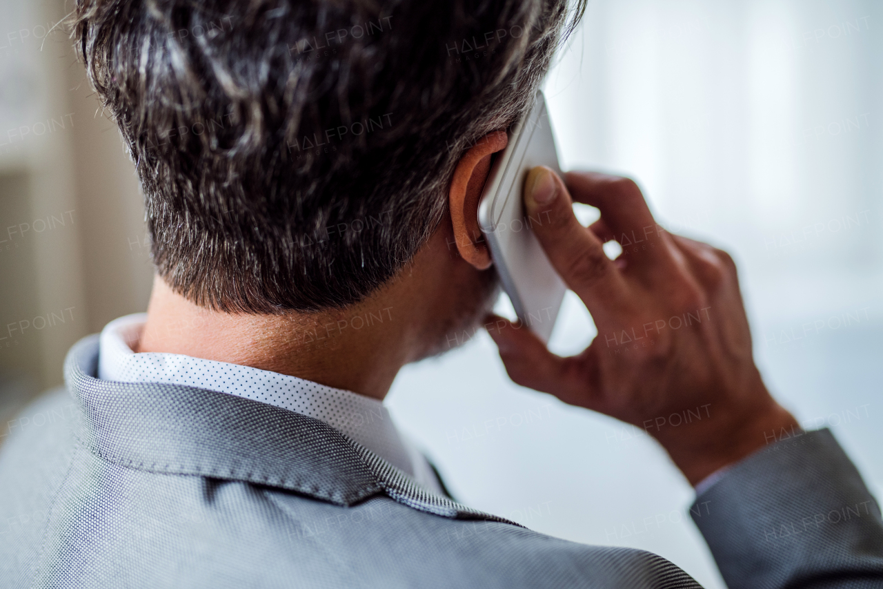 A rear view of mature businessman with smartphone making a phone call. A close-up.