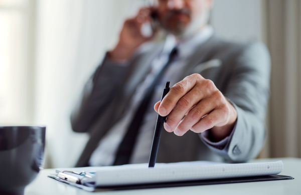 A midsection of unrecognizable businessman with smartphone sitting at the table in an office, making a phone call.