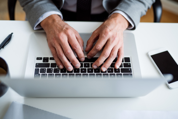 A midsection of businessman with laptop sitting at the desk in an office, working. A top view.