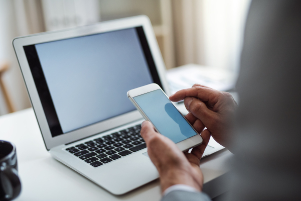 A midsection of businessman with smartphone and laptop sitting at the table in an office, working. Copy space.