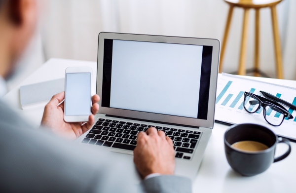 A midsection of businessman with smartphone and laptop sitting at the table in an office, working. Copy space.