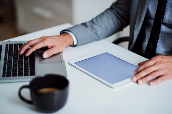 A midsection of unrecognizable businessman sitting at the table, using tablet. Copy space.