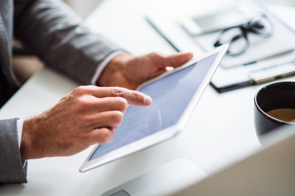 A midsection of unrecognizable businessman sitting at the table, using tablet. Copy space.