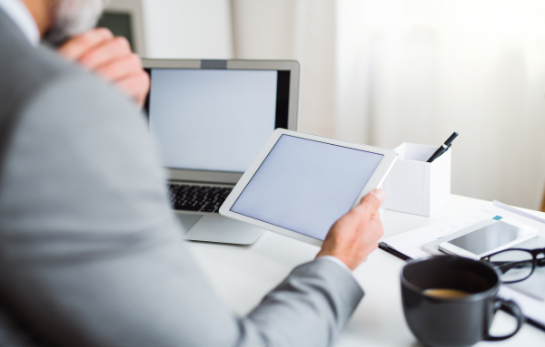 A midsection of unrecognizable businessman sitting at the table, using tablet. Copy space.