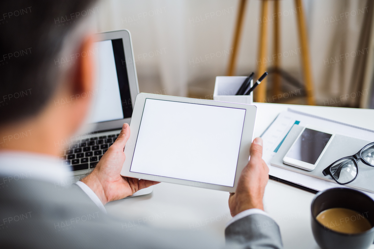 A midsection of unrecognizable businessman sitting at the table, using tablet. A rear view. Copy space.