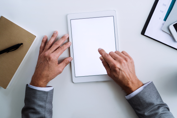 A midsection of unrecognizable businessman sitting at the table, using tablet. A top view. Copy space.