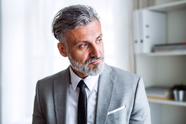 A serious mature businessman standing in an office, looking away.